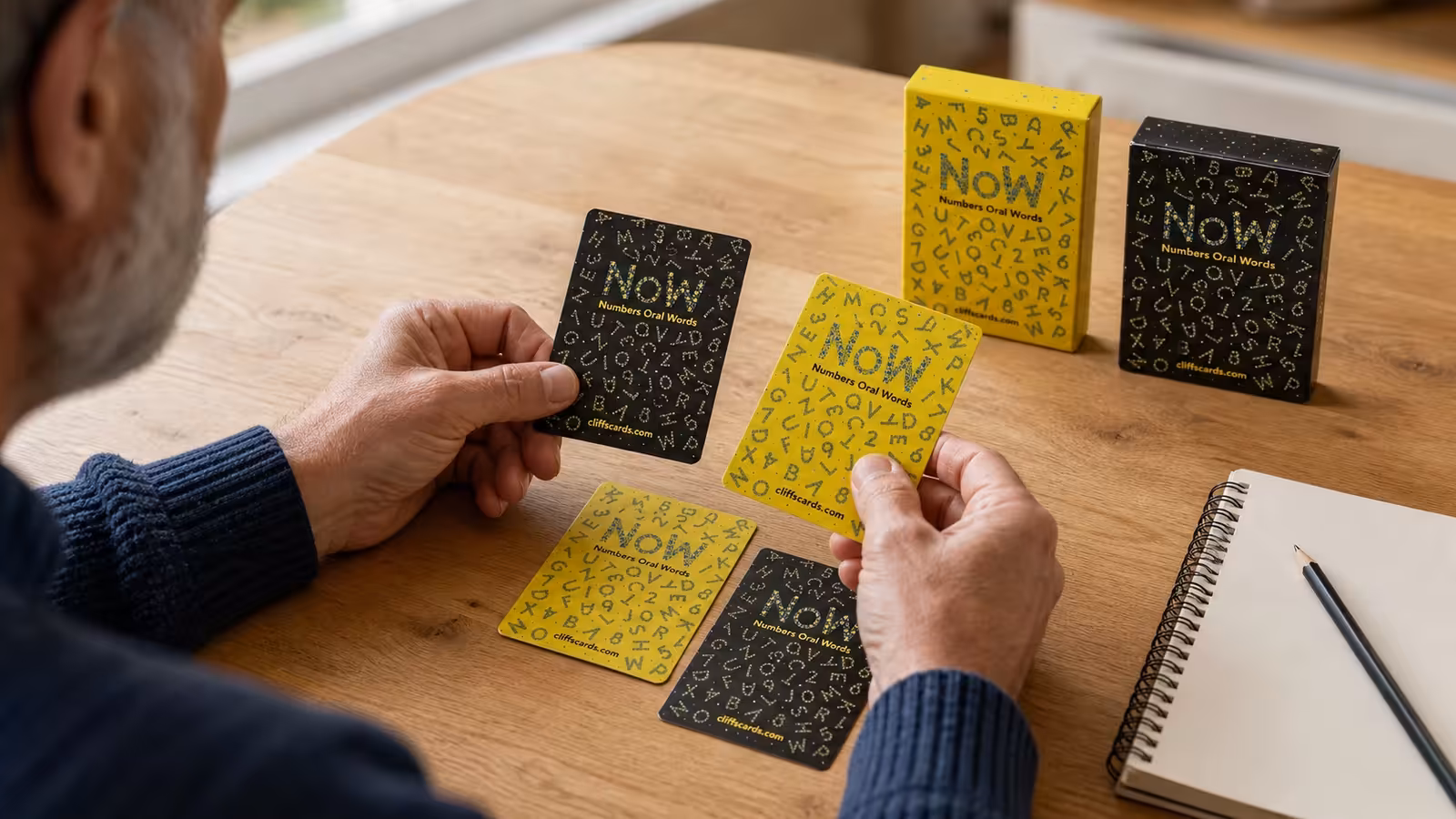 Older man arranging black and yellow NoW cards beside a notebook.